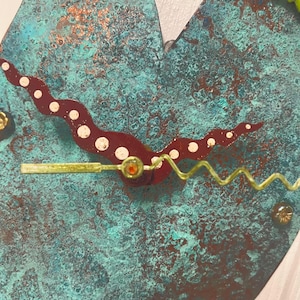 May include: A heart-shaped wall clock with a textured, oxidized copper-green and brown patina finish. The clock features a wavy, dark red hour hand with white dots and a thin, zigzagging lime green minute hand, with a small green lizard figure.
