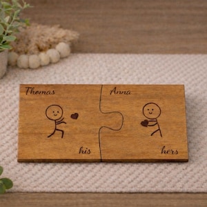 May include: Two rectangular wooden puzzle pieces that fit together. The left piece is engraved with the name Thomas, a stick figure, and the word his. The right piece is engraved with the name Anna, a stick figure holding a heart, and the word hers.