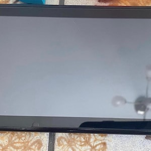 May include: Black handheld games console with a large screen and attached controllers. The console has buttons and a joystick on each controller. The screen is reflective, and the console is lying flat.