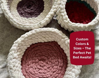 May include: Three handmade pet beds in varying colors. The beds are circular, with a thick, textured white yarn exterior and a contrasting interior. One bed has a purple center, another a red center, and the third a pink center. The beds are on a patterned surface.