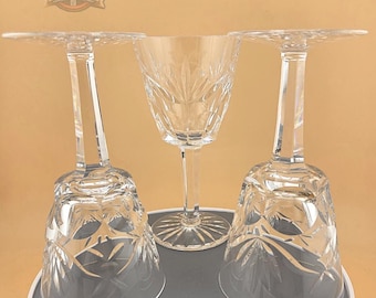 Könnte beinhalten: Drei klare Kristall-Weingläser mit aufwendigen Schliffmustern. Zwei Gläser sind umgedreht und zeigen das detaillierte Design der Schale. Das dritte Glas steht aufrecht und zeigt Stiel und Fuß. Die Gläser stehen auf einer grauen Oberfläche.