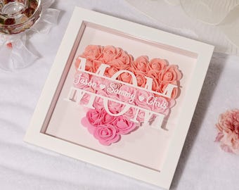 Può includere: Cornice bianca con un'arrangiamento a forma di cuore di rose artificiali rosa e pesca. La parola "MOM" è tagliata fuori dalla cornice e i nomi "Jason", "Sammy" e "Chris" sono scritti sotto la parola "MOM".