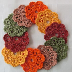 May include: A set of ten crocheted flower doilies in shades of orange, red, brown, and green. The doilies are arranged in a circle, with the largest doily in the center and the smallest doilies on the outside.