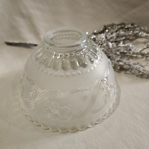 May include: A frosted glass lampshade with a scalloped edge and floral design. The clear glass rim is decorated with small, round beads. The shade has a soft, diffused appearance, and the floral pattern is etched into the glass.