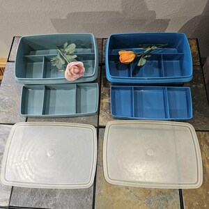 May include: Four plastic storage containers in shades of blue and teal, with matching lids. Two containers have dividers, and one has a pink rose. The other has an orange rose. The lids are off-white.