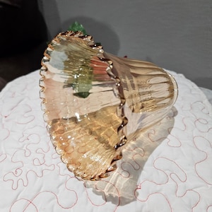 May include: A decorative, amber-colored glass bowl with a ruffled edge. The bowl has a textured surface and a flared shape. The rim is a darker shade of amber. The bowl is sitting on a white quilted surface.