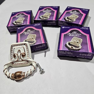 May include: Five Regency White bail pulls from The Bonaventure Collection, with matching boxes. The pulls are white with gold accents and a decorative design. Each box is purple with white text.