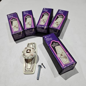 May include: Five boxes and a cabinet knob with backplate. The boxes are black and purple with the text "The Bonaventure Collection" and "C-274-RW Knob/Backplate". The knob is white with a decorative design and a square center. A screw and a nail are also present.