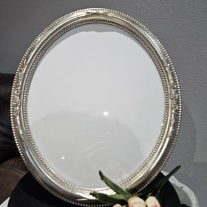 May include: A silver-colored, oval-shaped tray with a decorative beaded edge. The tray has a reflective surface and is set against a neutral background. The tray is likely used for serving or display purposes.