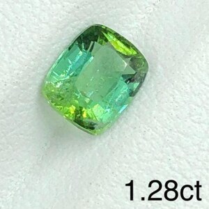 May include: A faceted, cushion-cut gemstone displaying a mix of green and teal colours. The gem is set against a white backdrop. The text "1.28ct" is visible, indicating the carat weight of the stone.