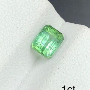 May include: A rectangular, light green gemstone with visible internal structures. The gem is set against a white background and the text "1ct" is visible in the lower right corner. The gemstone appears to be faceted.