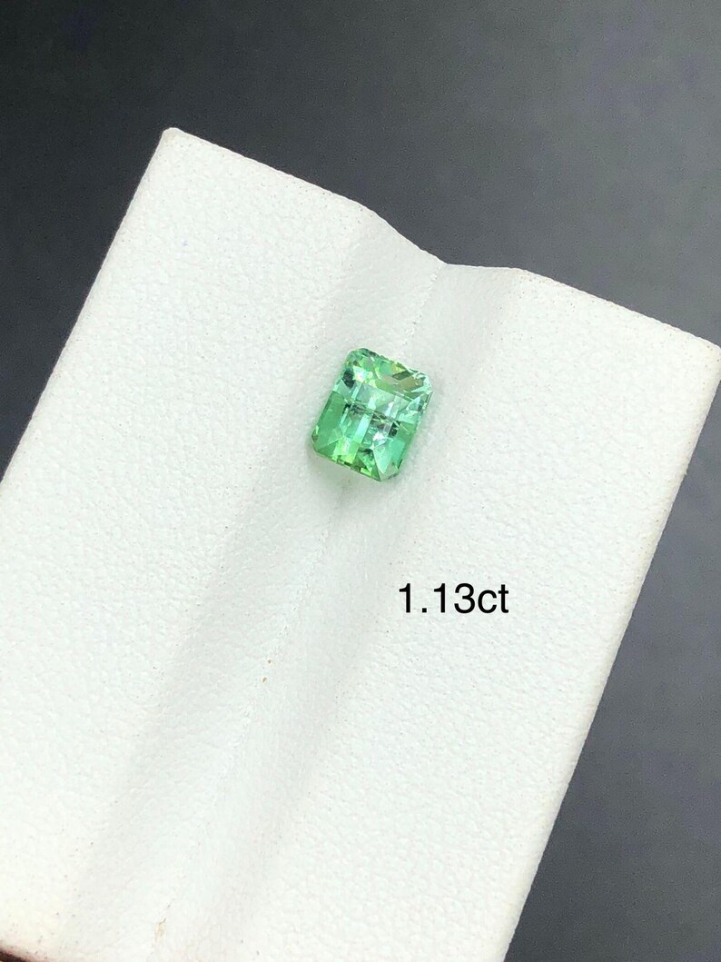 May include: A bright green, rectangular gemstone on a white surface. The gem is a clear, vibrant green. The text "1.13ct" is printed below the gemstone. The gemstone's weight is 0.226 grams.