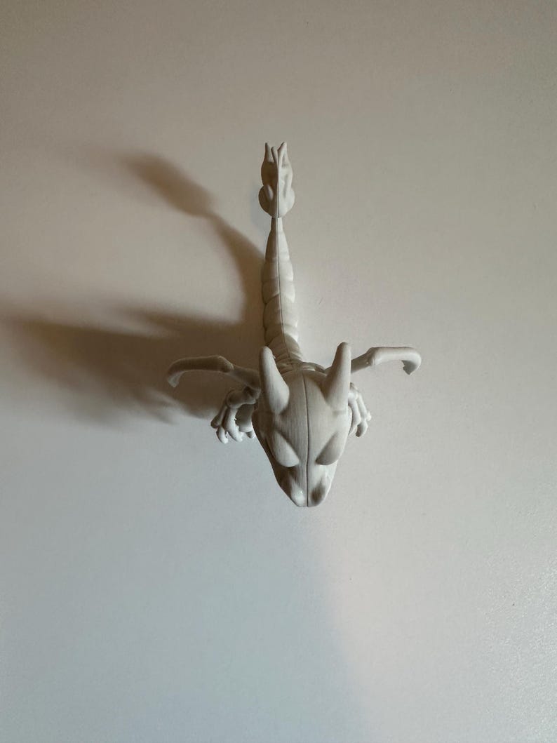 Peut inclure: Figurine de scorpion gris clair, stylis&eacute;e, avec un corps segment&eacute; d&eacute;taill&eacute;, des pinces et une queue incurv&eacute;e. Le scorpion a une t&ecirc;te d&eacute;taill&eacute;e avec de grands yeux ovales et deux cornes. La figurine est pos&eacute;e sur un fond blanc uni.