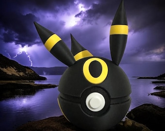 Könnte beinhalten: Eine 3D-gedruckte Pokémon-Figur in Schwarz und Gelb, die einem Pokémon vom Typ Unlicht ähnelt und wie ein Pokéball mit Ohren aussieht. Die Figur ist vor einem dunkelblauen Hintergrund mit Blitzen platziert.