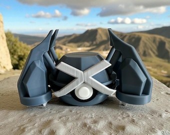 May include: A 3D-printed, blue and white Metagross figure. The figure has a geometric design with a white X-shaped pattern on the front. The figure is set against a backdrop of mountains and a cloudy sky.