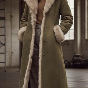 Könnte beinhalten: Ein langer, olivgrüner Mantel mit Kapuze und Manschetten mit Fellfutter. Der Mantel hat eine Knopfleiste und einen Fellbesatz. Das Model trägt einen braunen Rollkragenpullover und eine karierte Hose. Ein stilvolles Oberbekleidungsstück.