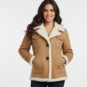 Puede incluir: Chaqueta color canela con forro y ribete de color crema y peludo. La chaqueta tiene dos bolsillos delanteros, cierre de botones y cuello. La modelo lleva la chaqueta con vaqueros azul oscuro.