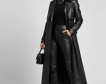 Op de afbeelding: Een lange zwarte leren trenchcoat, gecombineerd met een zwarte coltrui, broek en laarzen met hakken. De outfit wordt gecompleteerd met een kleine zwarte handtas en zonnebril. De jas heeft een klassieke trenchcoat-stijl.