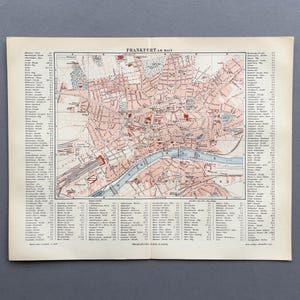 Puede incluir: Mapa antiguo de Frankfurt am Main, Alemania, con un plano detallado de las calles en tonos rojos y rosas. El mapa incluye un río azul y numerosos nombres de calles a los lados. El título "Frankfurt am Main" está impreso en la parte superior.