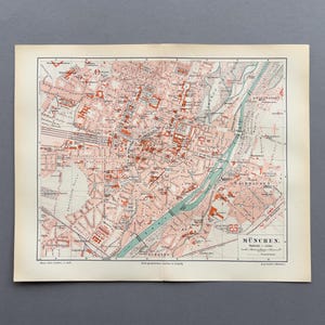 Peut inclure: Carte ancienne de Munich, Allemagne, avec un plan de la ville détaillé en rouge, rose et vert. La carte comprend les rues, les bâtiments et une rivière, avec le nom de la ville en bas. Imprimée sur du papier vieilli.