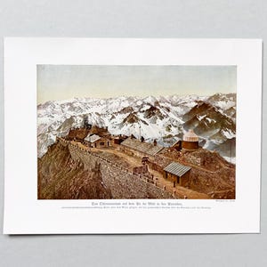 May include: A vintage colorized print depicting the Pic du Midi Observatory in the Pyrenees mountains. The image shows stone buildings and a domed structure perched on a rocky ridge, with snow-capped mountain peaks in the background.
