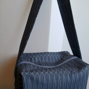 May include: A dark blue fabric tote bag with a white patterned design. The bag has a zipper closure and a long strap.