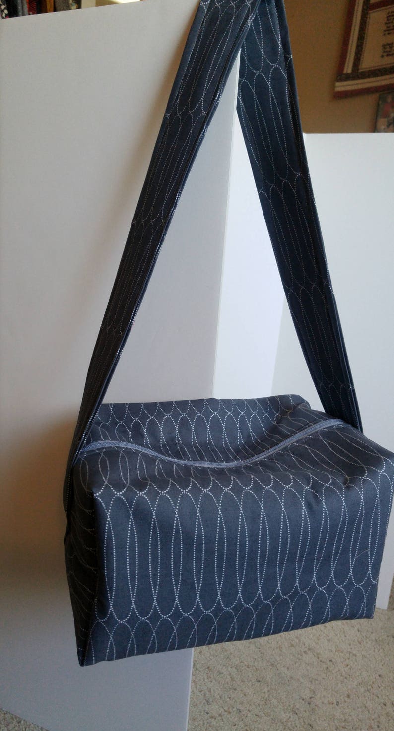 May include: A dark blue fabric tote bag with a white patterned design. The bag has a zipper closure and a long strap.