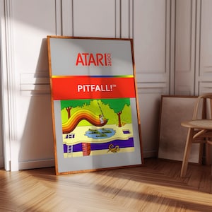 Op de afbeelding: Een vintage Atari 2600 videospelcartridge met een rood label waarop "PITFALL!" in witte letters staat. De spelkunst toont een cartoonfiguur dat aan een liaan schommelt boven een waterpoel met alligators.