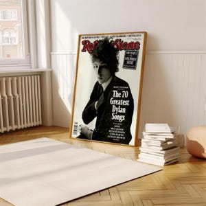 May include: A magazine cover featuring a black and white photo of Bob Dylan. The magazine is titled "Rolling Stone" and the headline reads "The 70 Greatest Dylan Songs".