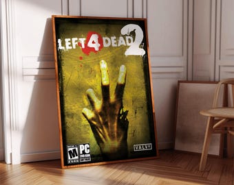 May include: Framed poster for the video game "Left 4 Dead 2." The artwork features a hand with three fingers raised against a yellow and green background. The game's title is displayed in white and red letters. The poster is in a wooden frame.