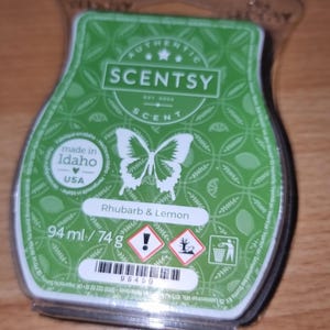 Könnte beinhalten: Grünes Scentsy-Duftwachs mit Schmetterlingsdesign und der Aufschrift "Rhubarb & Lemon". Die Verpackung enthält 94 ml / 74 g. Hergestellt in Idaho, USA. Mit Barcode und Gefahrensymbolen.