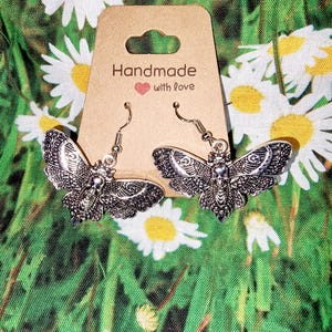 Könnte beinhalten: Silberne Schmetterlings-Ohrringe mit filigranen Details. Die Ohrringe befinden sich auf einer braunen Karte mit dem Text "Handmade with love".
