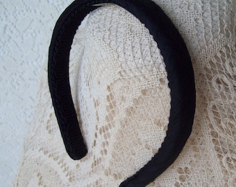Puede incluir: Una diadema de terciopelo negro con un borde decorativo. La diadema está sobre un fondo de encaje blanco.