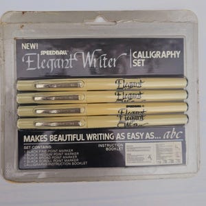Op de afbeelding: Een set van vijf zwarte kalligrafie-stiften in een doorzichtige plastic verpakking. De stiften zijn gelabeld met "Elegant Writer" en "Speedball". De verpakking bevat ook een instructieboekje. De set bevat een fijne punt, een middelpunt, een brede punt, een rolpunt en een kalligrafie-instructieboekje.