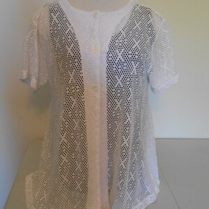 May include: White crochet top with a button-up front and a diamond pattern. The top has short sleeves and a loose fit.