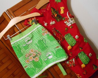 May include: Two kitchen aprons hanging on a wooden rack. The top apron is red with a white and green floral pattern. The bottom apron is green with a white and green checkered pattern.