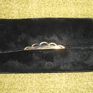 May include: A black velvet clutch purse with a gold metal clasp. The clasp has a decorative design of five rounded arches.