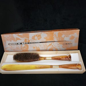 May include: A vintage "Porch Set" in a box, featuring a brush and a shoe horn. The brush has dark bristles and a wooden handle with gold-colored accents. The shoe horn is a similar design. The box has an orange and white design.