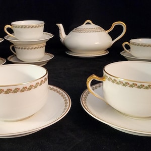 May include: A set of white porcelain teacups and saucers with gold trim and a matching teapot. The cups and saucers have a delicate floral design.