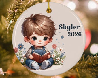 May include: A round white ceramic ornament featuring a cartoon illustration of a child with brown hair wearing blue overalls and reading a red book. The ornament is decorated with colorful flowers and includes the text Skyler and the year 2026.