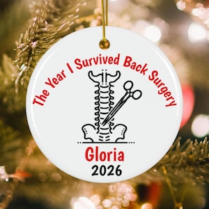 May include: A round white ceramic ornament featuring a black line drawing of a human spine with surgical scissors. The red text reads The Year I Survived Back Surgery, with the name Gloria in red and the year 2026 in black printed below.