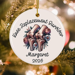 May include: A round white ceramic ornament featuring a graphic of two anatomical knee joints surrounded by colorful flowers. The text reads Knee Replacement Survivor, Margaret, and 2026 in black script. A gold string is attached to the top.