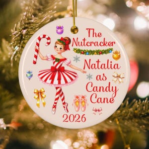 May include: A round white ceramic ornament featuring a ballerina in a red and white striped dress holding a candy cane. The text reads The Nutcracker Natalia as Candy Cane 2026. It includes illustrations of bows, ornaments, and ballet slippers.