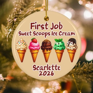 May include: A round, beige ceramic ornament featuring the text First Job Sweet Scoops Ice Cream, followed by five illustrated ice cream cones with various toppings, and the name Scarlette 2026 printed in dark red at the bottom with a gold string.