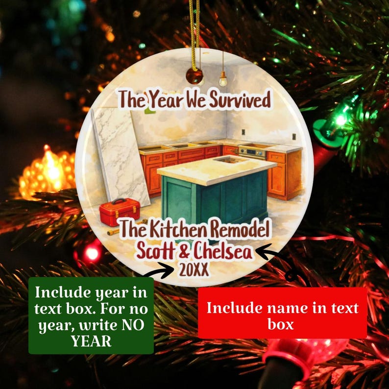 May include: A round ceramic ornament featuring an illustration of a kitchen remodel with orange cabinets, a teal island, and a red toolbox. The text reads: The Year We Survived, The Kitchen Remodel, Scott & Chelsea, 20XX. It hangs by a gold string.
