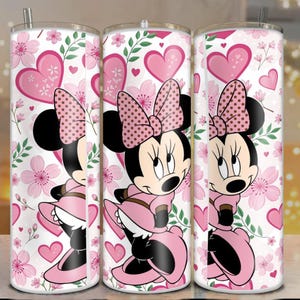 May include: Three stainless steel tumblers featuring a Minnie Mouse design. The design includes Minnie in a pink dress and bow, surrounded by pink hearts and flowers on a white background. Each tumbler has a silver straw.