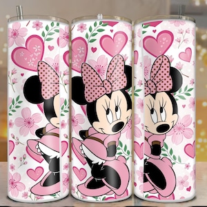 May include: Three stainless steel tumblers featuring a Minnie Mouse design. The design includes Minnie in a pink dress and bow, surrounded by pink hearts and flowers on a white background. Each tumbler has a silver straw.