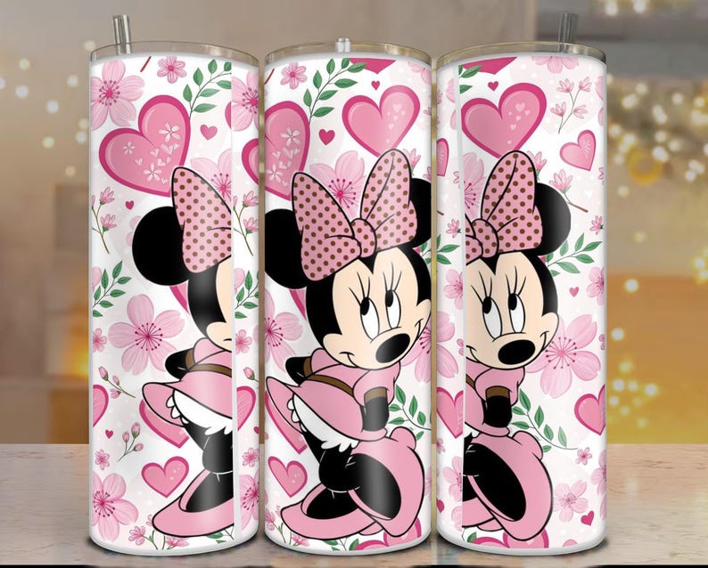 May include: Three stainless steel tumblers featuring a Minnie Mouse design. The design includes Minnie in a pink dress and bow, surrounded by pink hearts and flowers on a white background. Each tumbler has a silver straw.