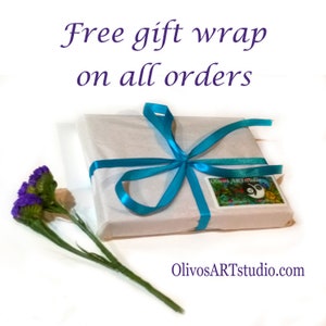 Puede incluir: Una caja de regalo blanca envuelta en una cinta azul con una peque&ntilde;a pegatina que dice "Olivos Art Studio" y un logotipo de oso panda. El texto "Free gift wrap on all orders" est&aacute; encima de la caja. La caja est&aacute; sobre una superficie blanca.