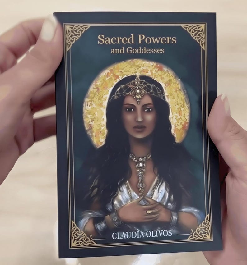A person's hands holding a book titled "Sacred Powers and Goddesses" by Claudia Oliveros.